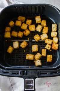 Cooked cubes of tofu in a black air fryer basket