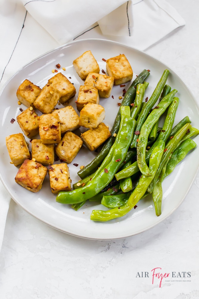 Vertical photo of a white plate containing air fried tofu cubes and green beans