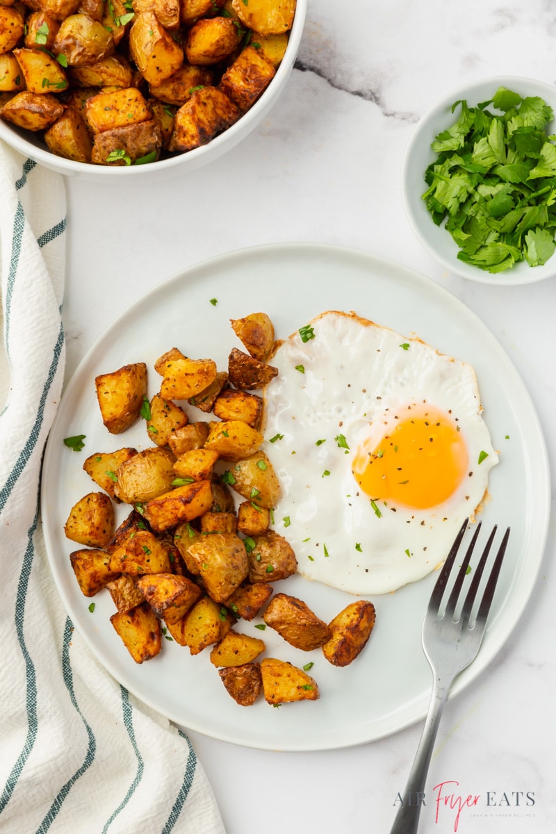 A white plate with a fried sunny side up egg and air fryer home fries on the side. 