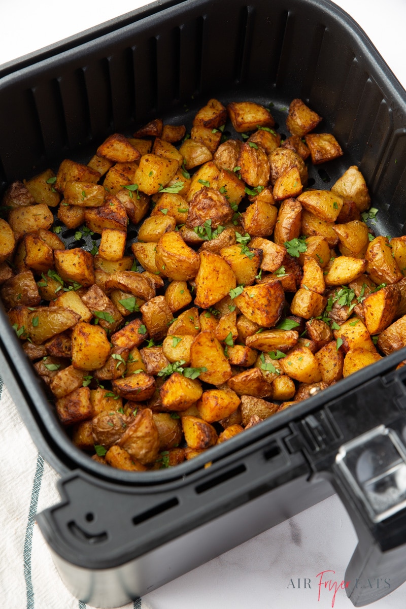 a cosori air fryer basket filled with cooked home fries, garnished with parsley