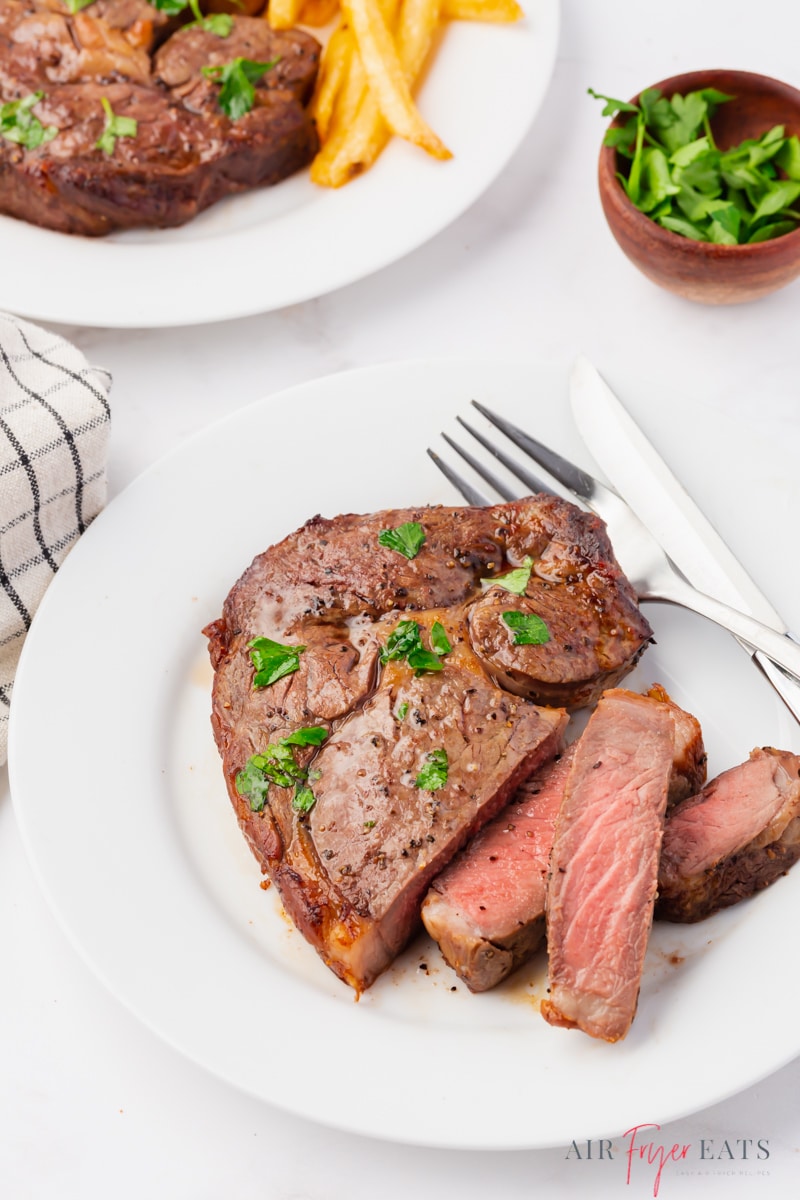 a perfectly cooked air fryer steak on a white dinner plate, garnished with parsley