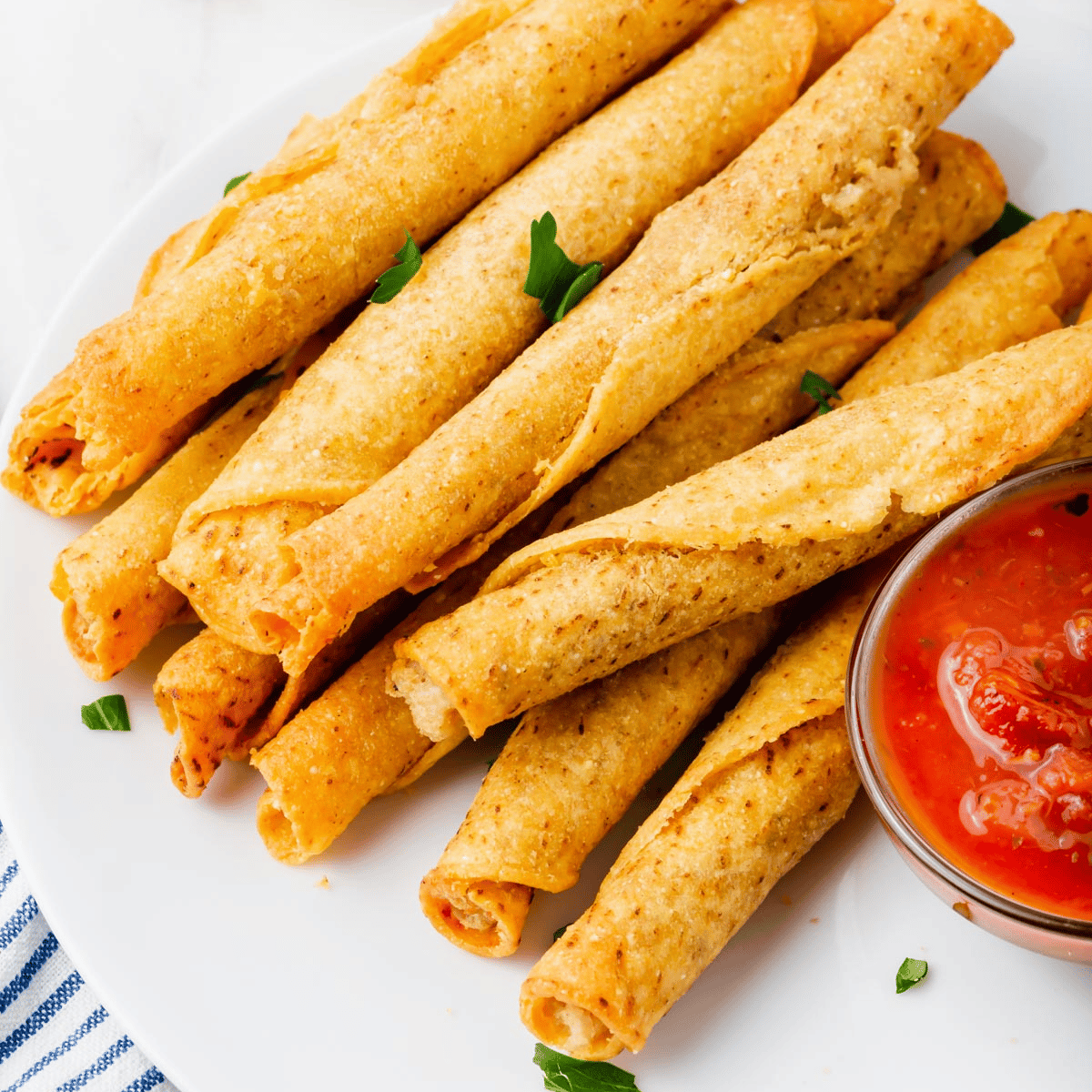 Taquitos that were cooked in an air fryer, on a plate with a side of sauce