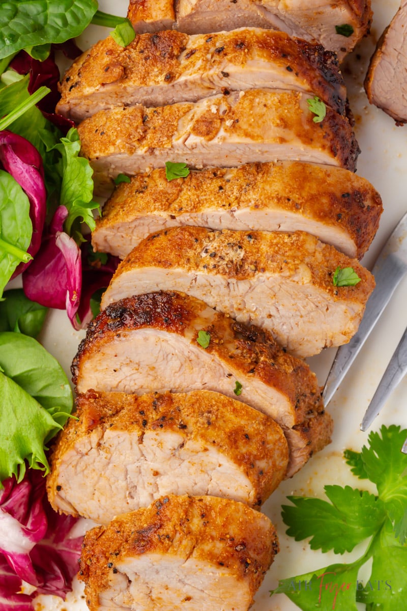 sliced pork tenderloin next to a green salad, garnished with parsley. 