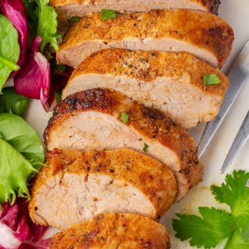 sliced pork tenderloin next to a green salad, garnished with parsley.