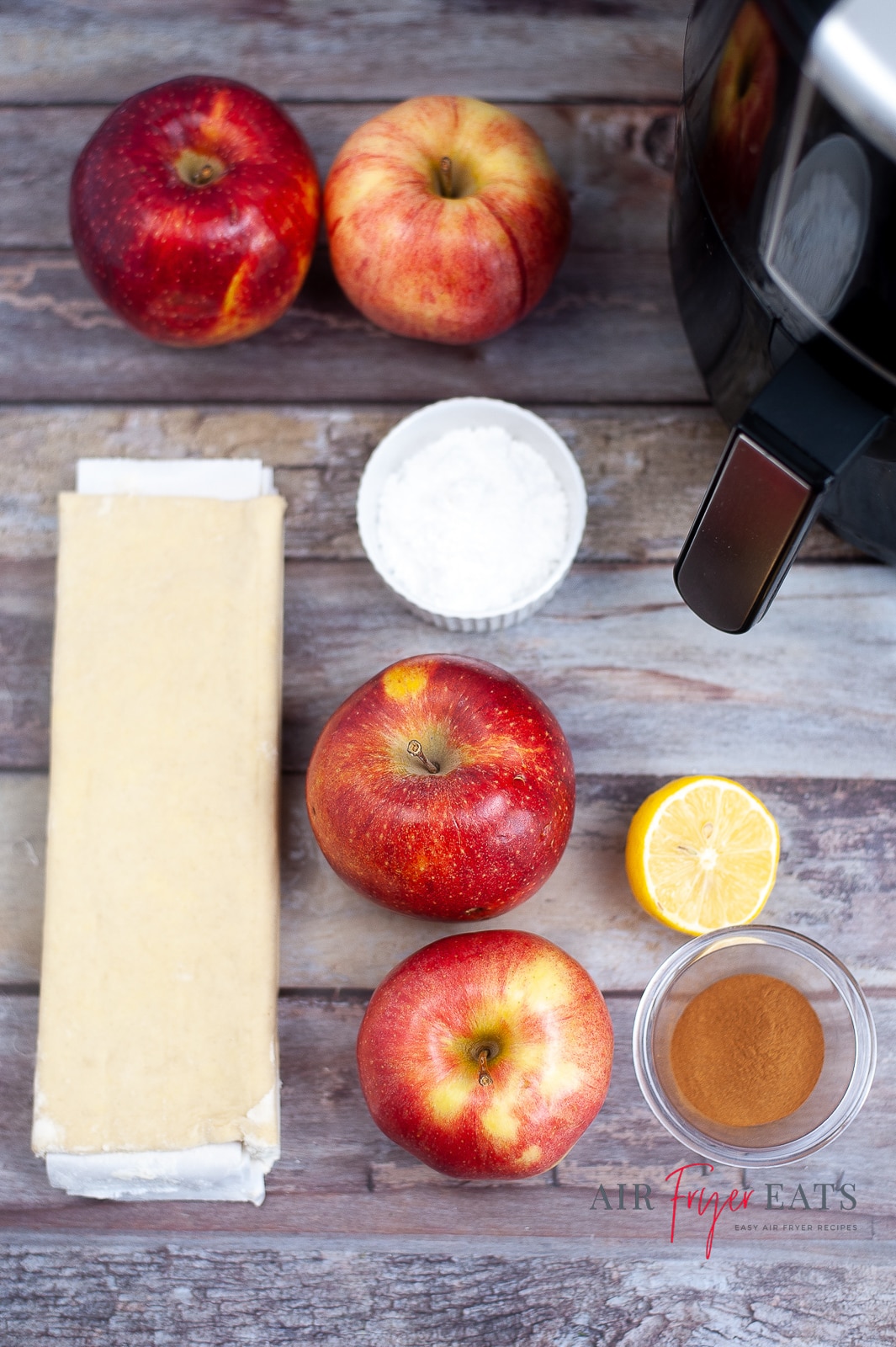 A vertical photo showing the ingredients required for air fryer apple roses. Puff pastry sheets, apples, lemon, sugar and cinnamon