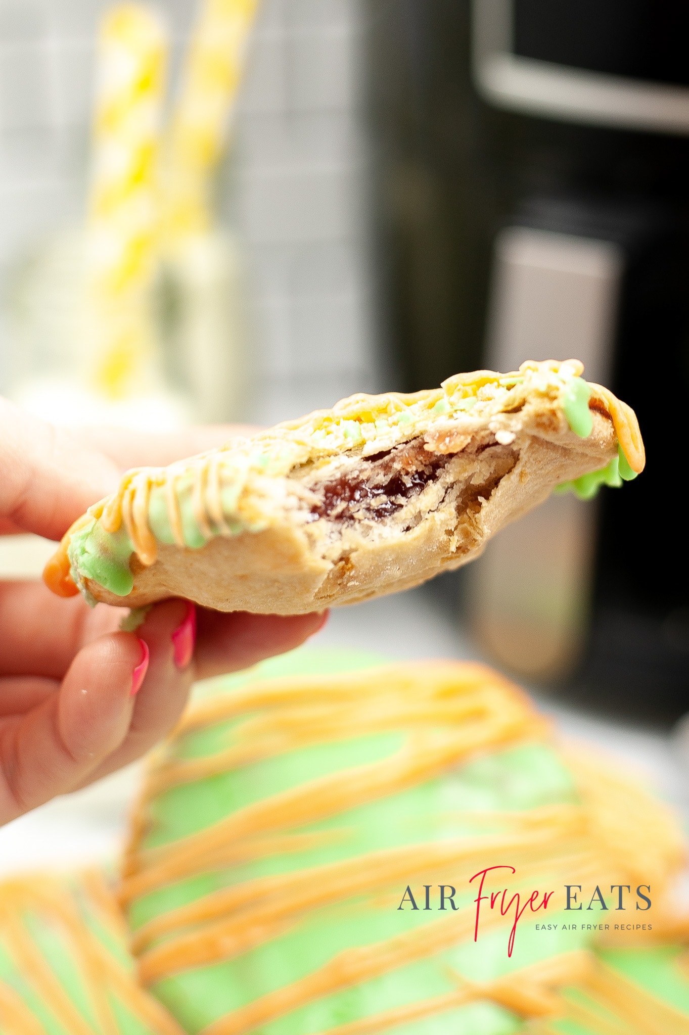 A hand holding a halloween poptart which has had a bite taken out of it. In the background is a black air fryer