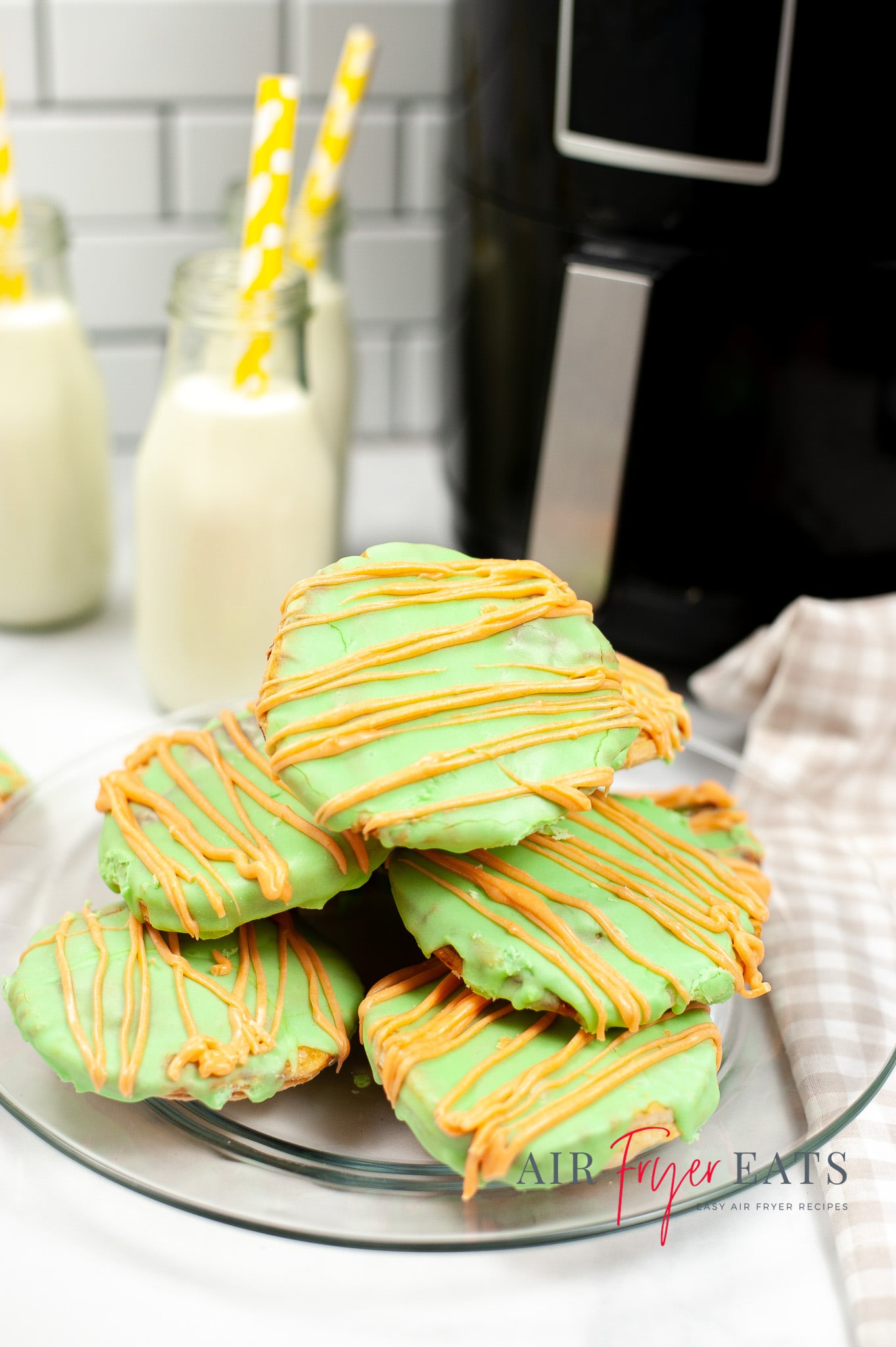 Vertical photo of a pile of green poptarts on a plate. In the background is a black air fryer and bottles of milk