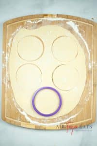 Dough rolled out on a floured surface, being cut into circles with a cookie cutter