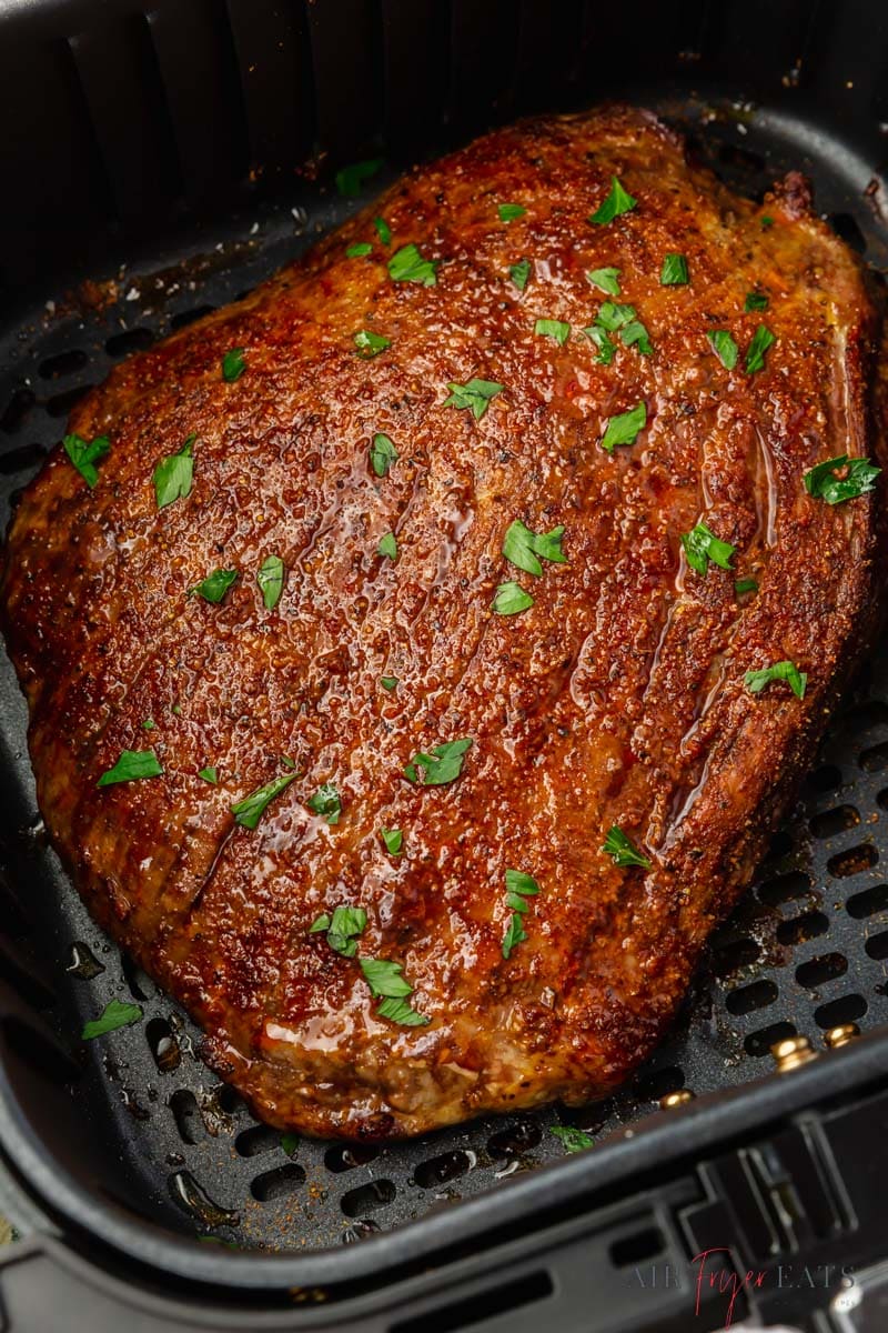 a large flank steak in a black square air fryer basket, cooked and garnished with fresh herbs.