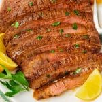 a large air fryer flank steak sliced, on a platter surrounded by lemon wedges.