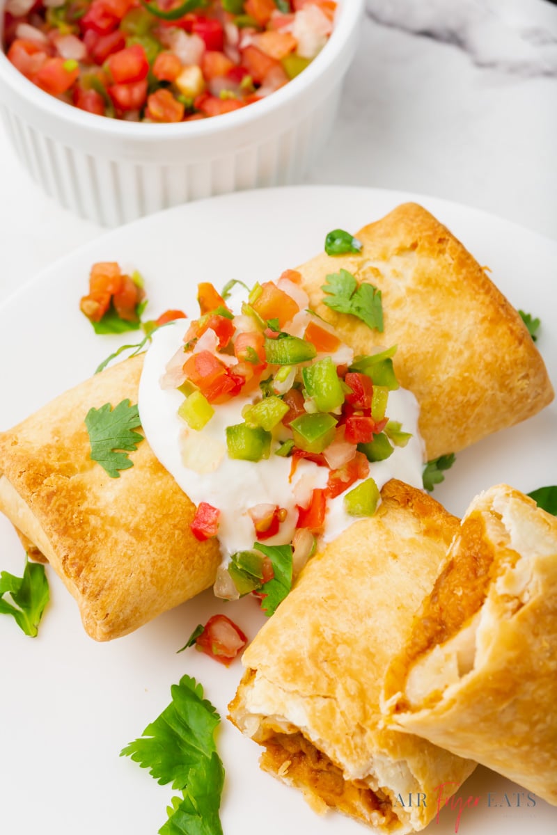 two crispy chimichangas topped with sour cream, salsa, and cilantro.