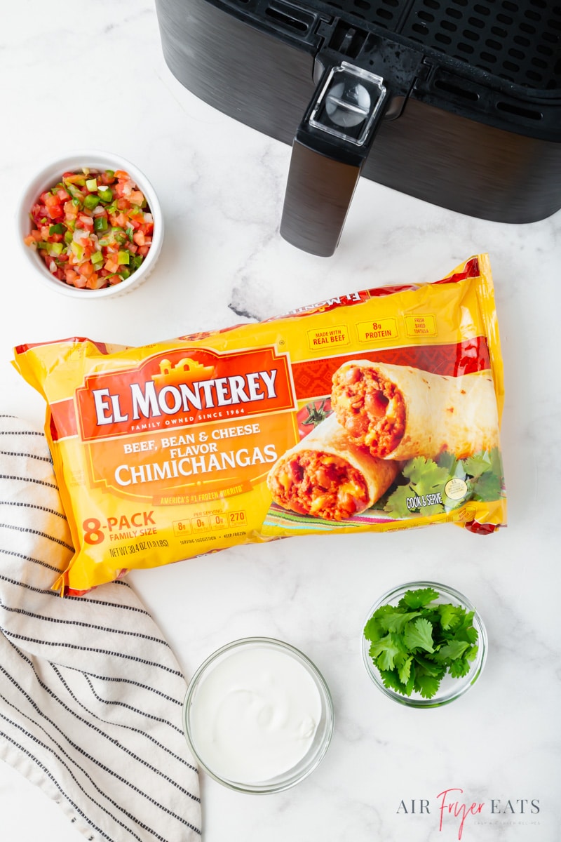 a frozen chimichanga and other ingredients next to an air fryer basket.