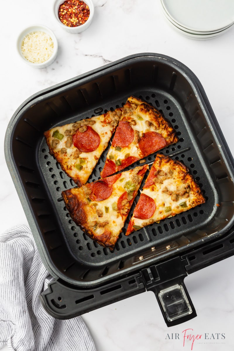 four slices of leftover pizza in a cosori air fryer basket, viewed from above