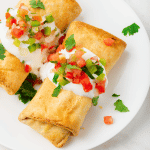 two crispy chimichangas topped with sour cream, salsa, and cilantro.