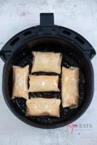 Black air fryer basket containing 5 egg rolls prior to air frying