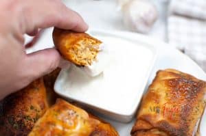 An egg roll being dipped in creamy white sauce