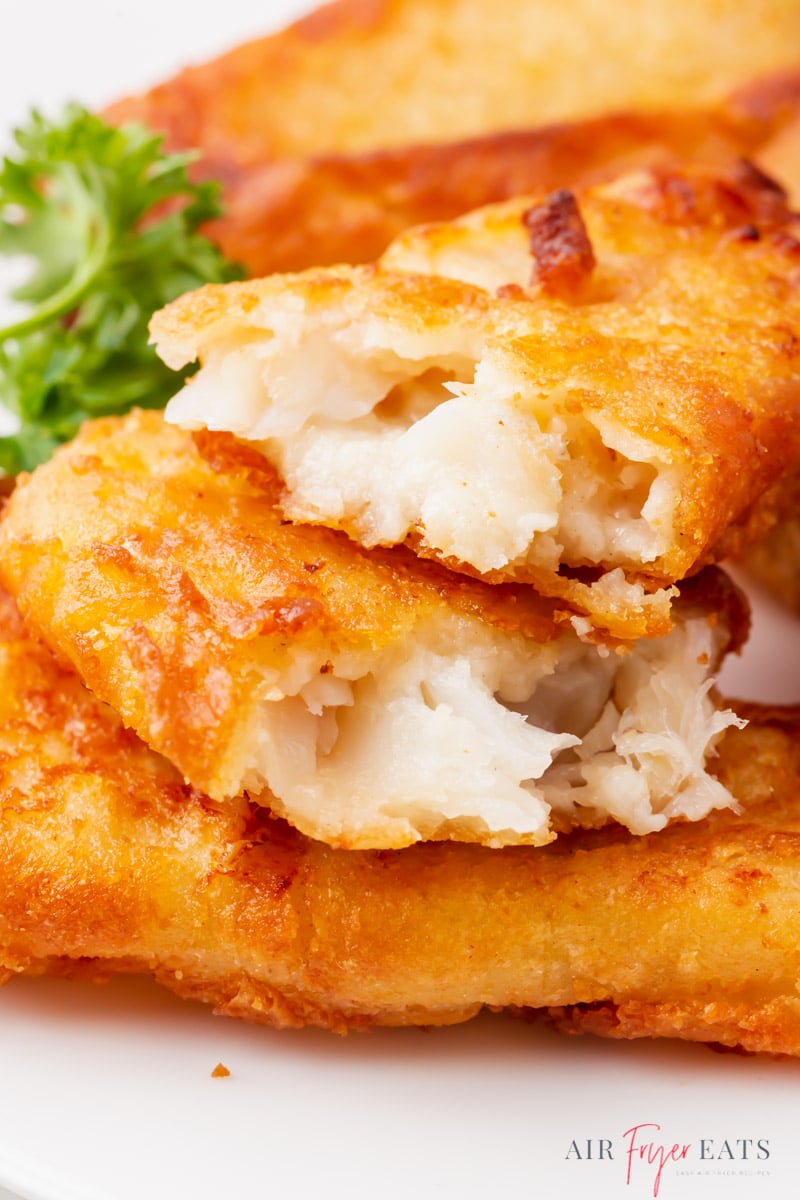 a stack of breaded fish on a plate. One has been broken in half to show the flaky interior.