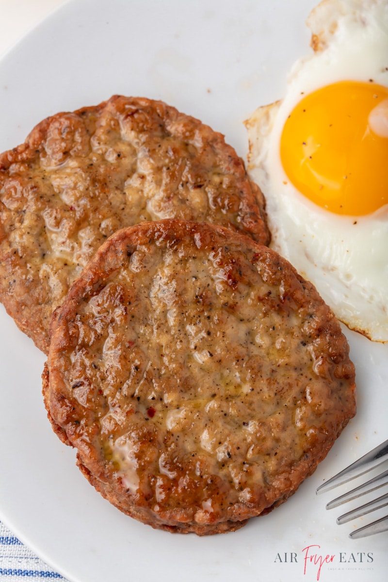 two large sausage patties on a plate next to a sunny side egg.