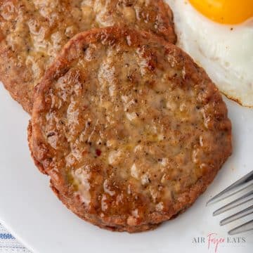 Sausage patties on a plate next to an egg.
