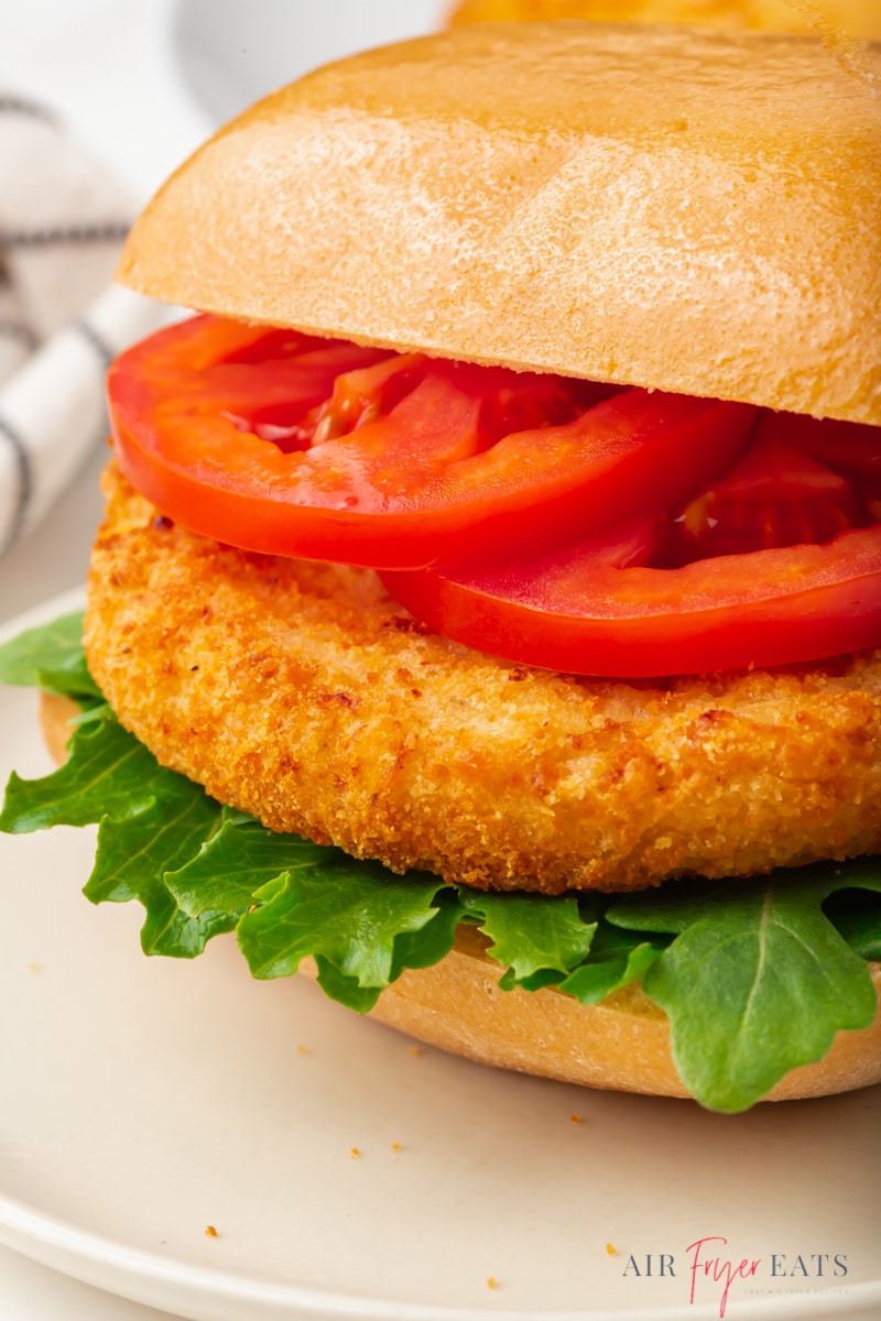  close up of a chicken patty sandwich on a square bun with lettuce and tomato slices.