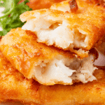 a stack of breaded fish on a plate. One has been broken in half to show the flaky interior.
