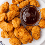 a plate of air fryer popcorn chicken with a small cup of barbecue sauce.