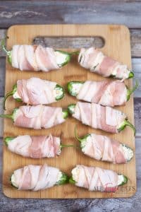 vertical photo of jalapeno halves with cheese mix and wrapped in bacon