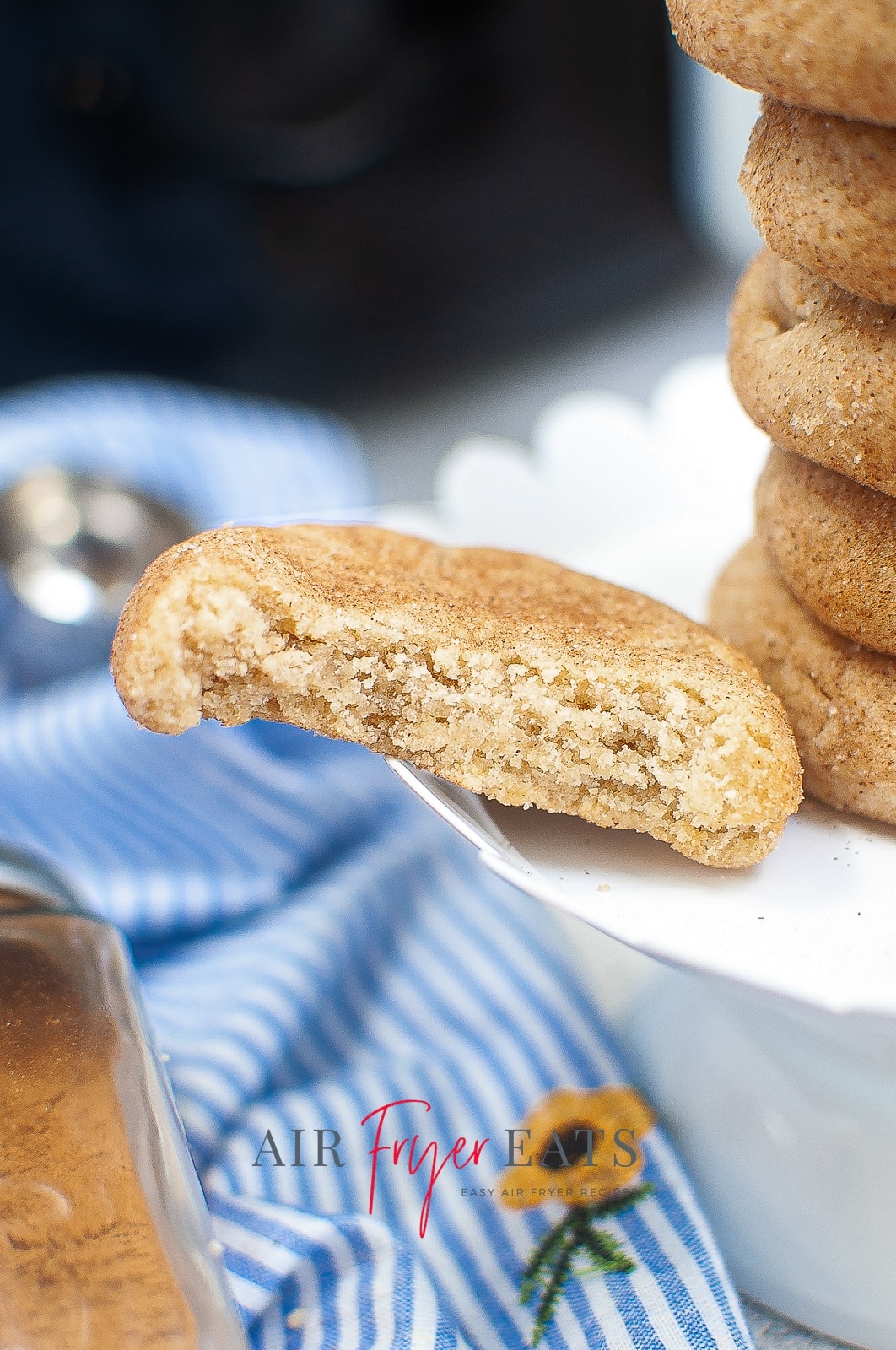 A half eaten snickerdoodle cookie resting against a stack of cookies on a white plate