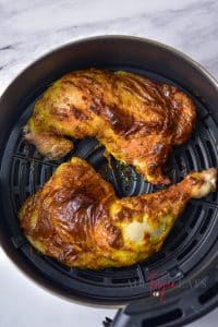vertical photo of 2 coated and cooked air fryer mustard chicken legs in the air fryer basket