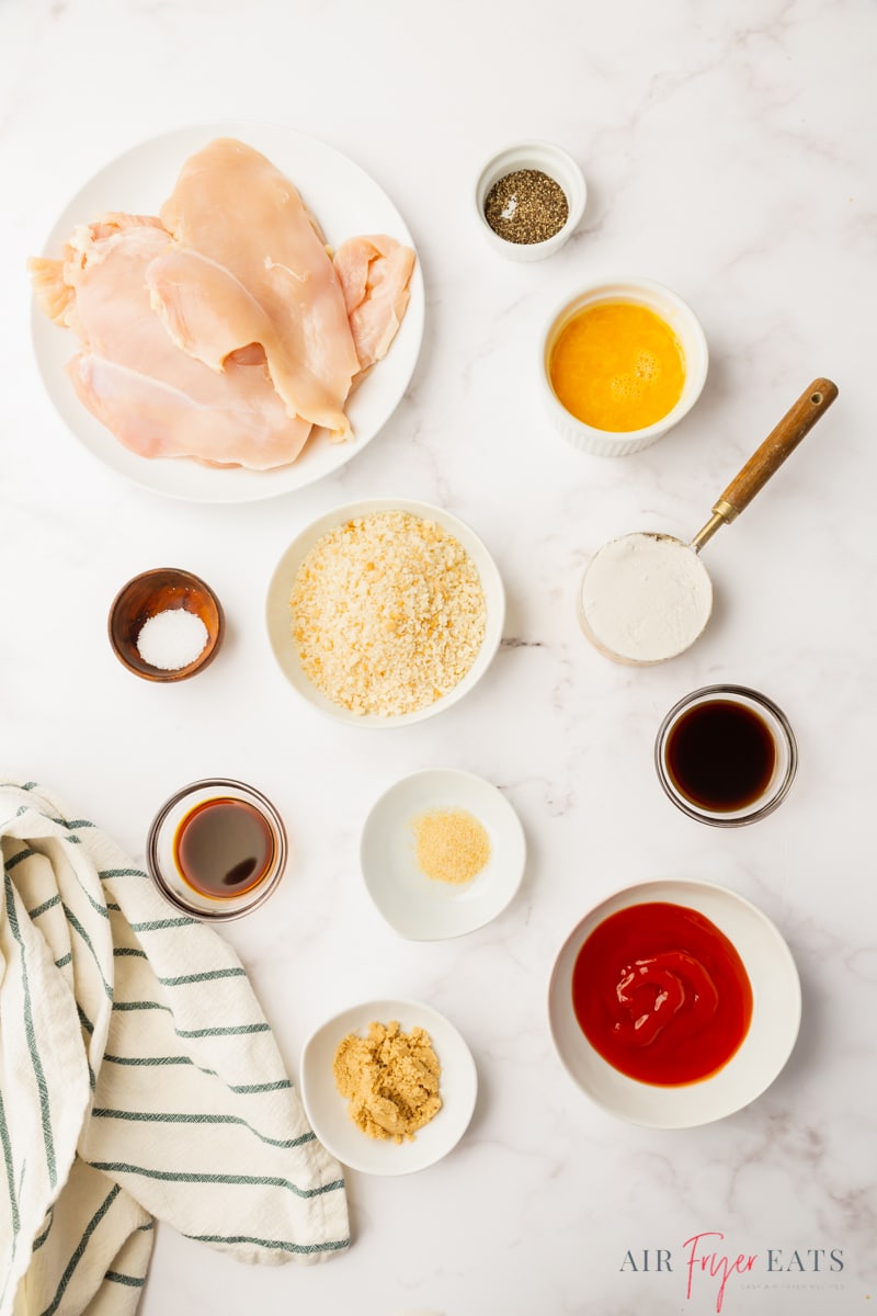The ingredients you need to make chicken katsu in the air fryer, all in separate bowls, arranged on a counter, viewed from above.