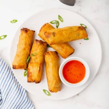 5 crispy spring rolls on a plate with sweet and sour sauce