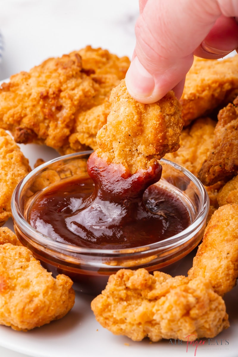 popcorn chicken being dipped into bbq sauce. 