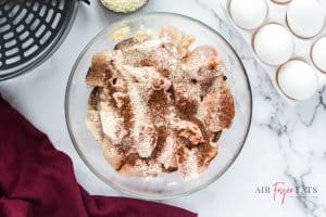 horizontal photo of cut chicken in a bowl with flour and spices added