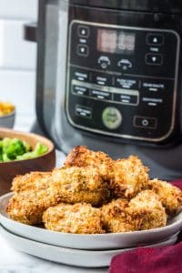 vertical photo of ninja foodi fried chicken in the foreground, air fryer broccoli and a ninja foodi