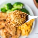 horizontal photo of a piece of fried chicken on a fork with a dinner plate in soft focus underneath
