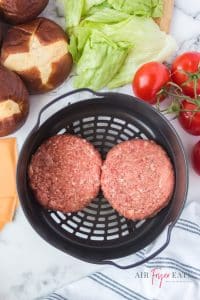 vertical photo of 2 burger patties in air fryer basket