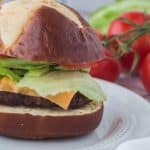 vertical photo showing ninja foodi air fryer burger with fresh fixings and cheese on a white plate with tomatoes and lettuce in the background