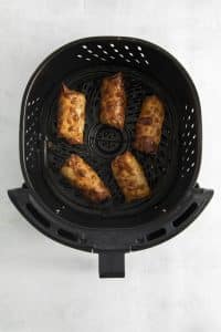 Top view photo of 5 fully cooked air fryer egg rolls in the air fryer basket.
