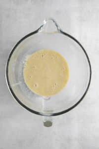 Top view photo of melted butter, egg, and vanilla in a stand mixer bowl with the yeast mixture, and mixed until combined.