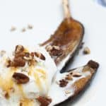 vertical photo showing air fryer glazed bananas on a white plate with ice cream and nuts topping