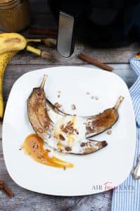 vertical photo of air fryer glazed bananas on a white plate with ice cream, nuts and caramel topping