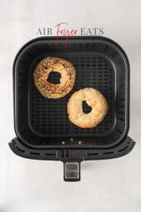 Top view photo of two air fryer bagels, air fried until golden brown, in the air fryer basket.
