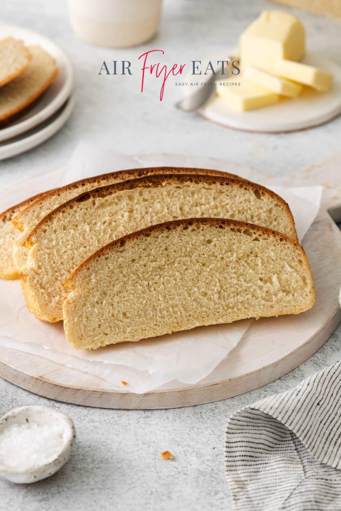 Photo of a sliced loaf of Air Fryer Bread, on a round cutting board. There is salt in the foreground and butter in the background.