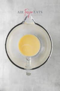 Top view photo of a glass mixing bowl with water, milk, butter, granulated sugar, and instant yeast, ready to mix.