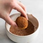 Photo of a hand dipping an Air Fryer Donut Hole into a small white bowl filled with a cinnamon-sugar topping.