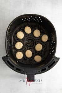 Top view photo of an air fryer basket filled with uncooked donut holes.