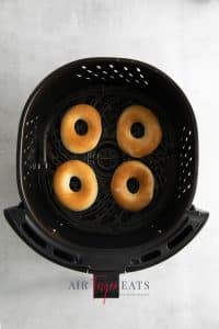 Top view photo of four air fryer doughnuts, in the air fryer basket and golden brown.