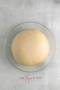 Top view photo of the dough for air fryer doughnuts, in a glass bowl, and fully risen.