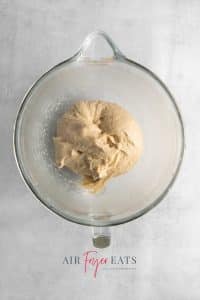 Top view photo of the dough for air fryer doughnuts, in a glass mixing bowl, and ready to shape for its rise.