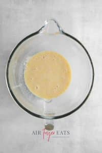 Top view photo of a glass mixing bowl with melted butter, egg, and vanilla added to the yeast and milk mixture.